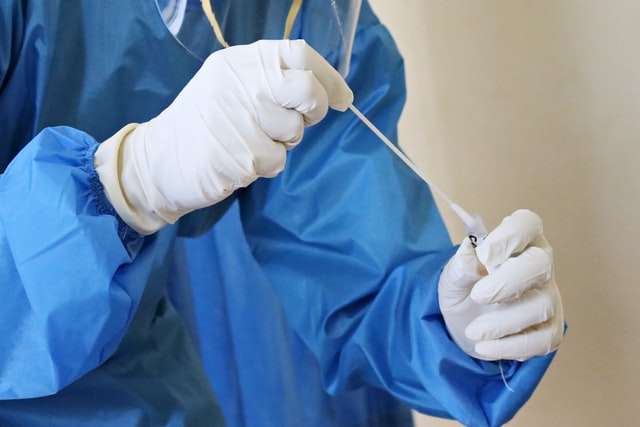 A medical professional in a PPE suit holding a swab test