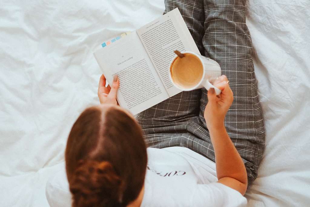Woman reading in bed with a cup of coffee